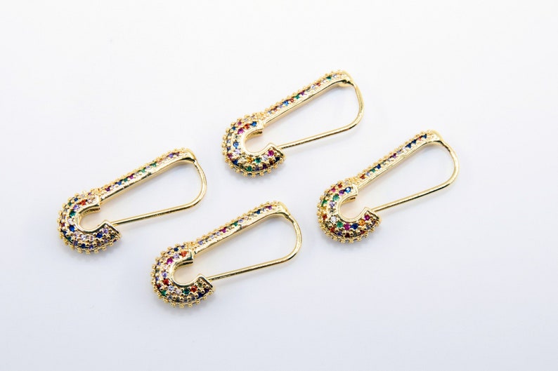May include: Four gold safety pin earrings with colorful rhinestones. The earrings are on a white background.