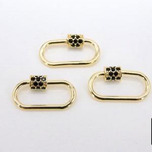 May include: Three gold-colored oval carabiner clasps with black cubic zirconia accents. The clasps have a rectangular center section encrusted with black stones. The clasps are on a white background. The logo of "A Girls Gems" is in the bottom right corner.