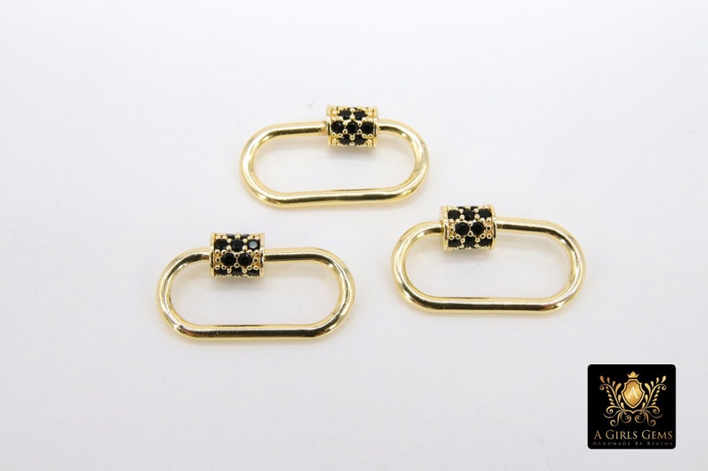 May include: Three gold-colored oval carabiner clasps with black cubic zirconia accents. The clasps have a rectangular center section encrusted with black stones. The clasps are on a white background. The logo of "A Girls Gems" is in the bottom right corner.