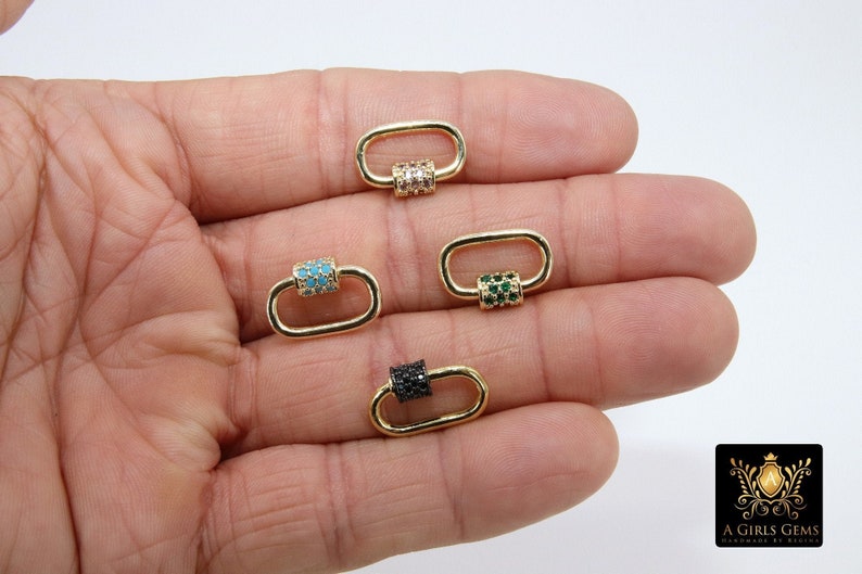 May include: Gold-colored oval-shaped clasps with various colored gemstone accents. The clasps feature accents in turquoise, clear, green, and black. The clasps are displayed on a hand against a white background. The logo "A Girls Gems" is in the bottom right corner.