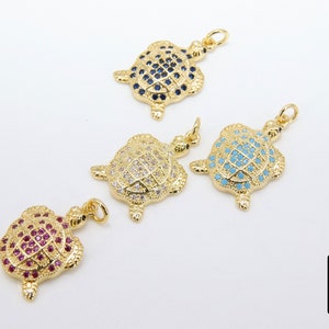 Op de afbeelding: Vier gouden schildpadbedels met verschillende gekleurde kristallen. De schildpadden zijn allemaal even groot en even gevormd, maar hebben verschillende gekleurde kristallen op hun schilden. De kristallen zijn blauw, wit, turquoise en roze.