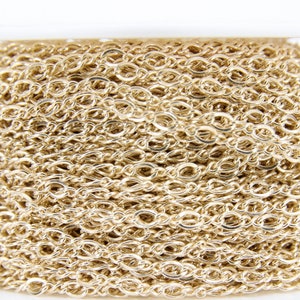 May include: A close-up of a spool of gold-colored chain. The chain is made of small, oval-shaped links.