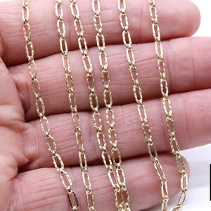 May include: A close-up of a gold chain necklace with a textured, oval-shaped link. The chain is laid out on a hand, showing the detail of the links.