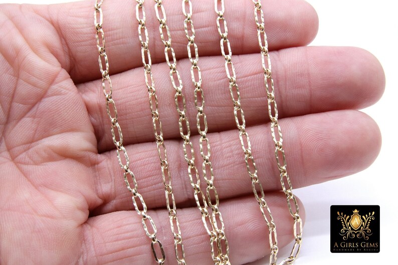 May include: A close-up of a gold chain necklace with a textured, oval-shaped link. The chain is laid out on a hand, showing the detail of the links.