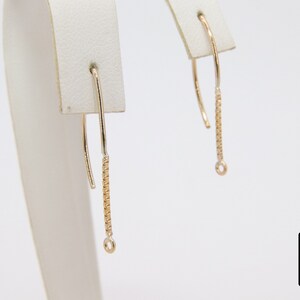 Pu&ograve; includere: Un paio di orecchini pendenti in oro con un delicato design a catena. Gli orecchini sono esposti su un espositore per gioielli bianco.