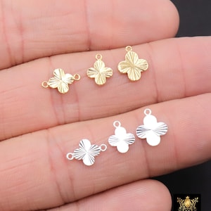May include: Gold and silver-colored clover-shaped charms. The charms have a textured surface and a small loop for attaching to jewelry. The image shows several charms in different sizes and finishes.