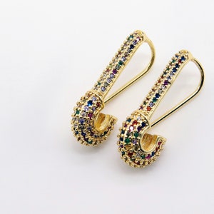 May include: A pair of gold safety pin earrings with colorful rhinestones.