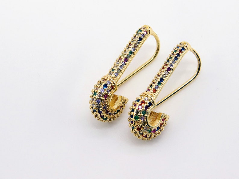 May include: A pair of gold safety pin earrings with colorful rhinestones.
