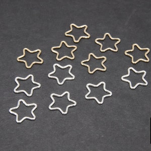 May include: A collection of silver and gold star-shaped jump rings. The jump rings are arranged in a circular pattern on a black background.