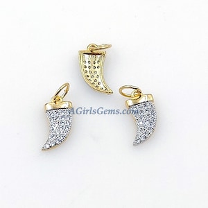 Puede incluir: Tres colgantes de color dorado en forma de colmillo curvo, cada uno con una piedra transparente de tipo cristal que cubre la superficie.  AGirlsGems.com está impreso en el fondo blanco.