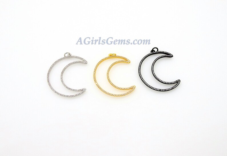 Pu&ograve; includere: Tre ciondoli a forma di mezzaluna con un unico anello in cima per l'appeso. I ciondoli sono in metallo e hanno una finitura argento, oro e nero. Ogni ciondolo &egrave; decorato con piccole pietre trasparenti.