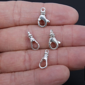 May include: Four silver-toned lobster claw clasps, commonly used for jewelry making.