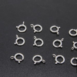 May include: Twelve silver-toned metal jump rings, each with a spring-loaded clasp. The rings are arranged in four rows of three.