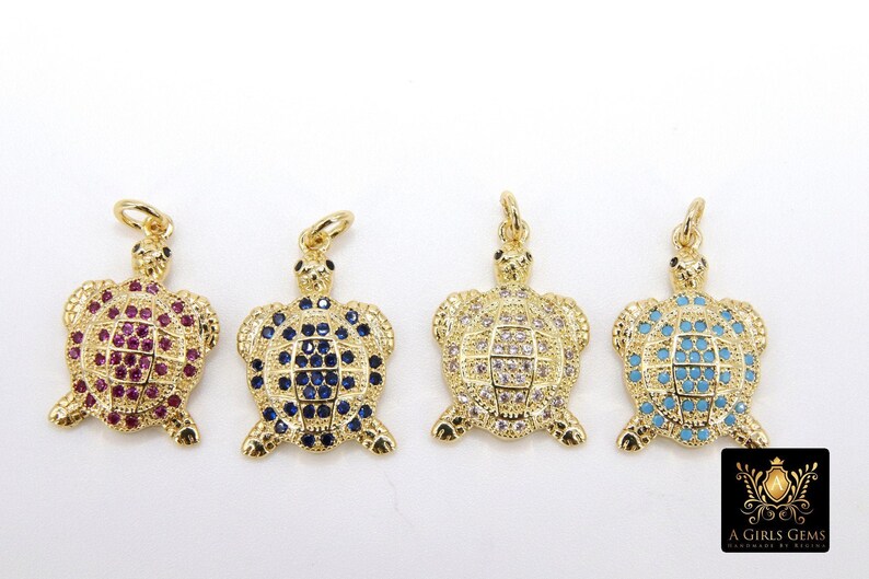 Op de afbeelding: Vier gouden schildpadbedels met verschillende gekleurde kristallen. De schildpadden zijn allemaal even groot en hebben dezelfde vorm, maar hebben verschillende gekleurde kristallen. De kristallen zijn rood, blauw, helder en turquoise.