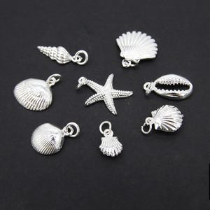 May include: A collection of silver-toned charms featuring various seashell designs, including a starfish, a cowrie shell, and a conch shell.