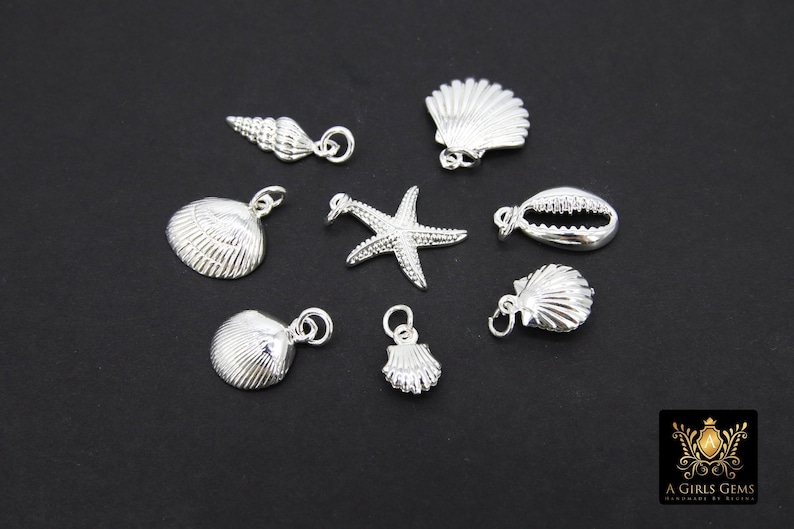 May include: A collection of silver-toned charms featuring various seashell designs, including a starfish, a cowrie shell, and a conch shell.