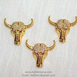 May include: Three gold-tone bull head charms with clear rhinestones. The charms are detailed with horns, eyes, and a nose.
