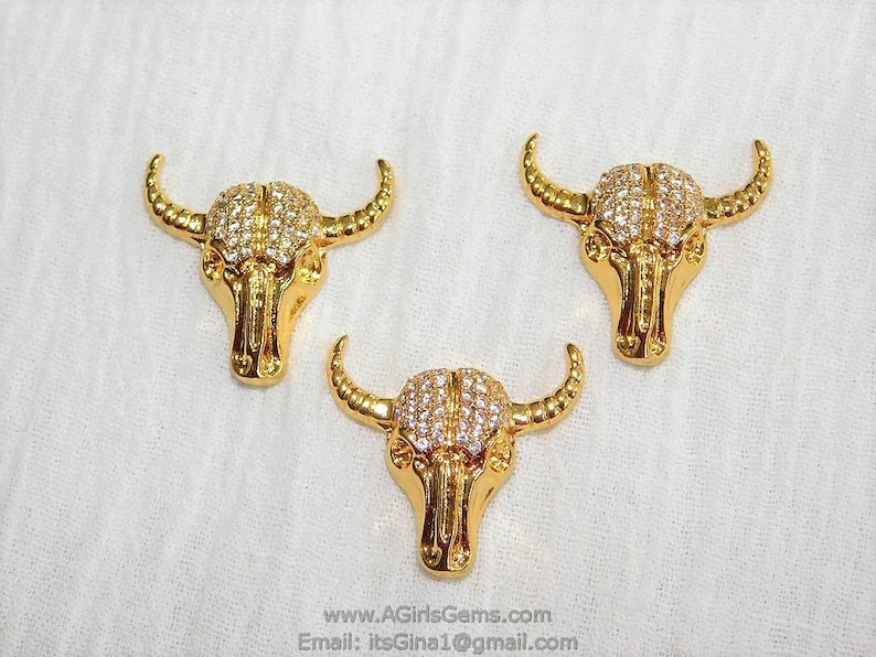 May include: Three gold-tone bull head charms with clear rhinestones. The charms are detailed with horns, eyes, and a nose.
