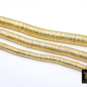 May include: A strand of gold-colored metal beads, each bead is a thin, flat disc with a slightly textured surface. The beads are arranged in a line, with the top row slightly overlapping the bottom row.