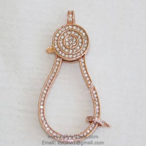 May include: A rose gold-toned clasp with a round, pave-set diamond design. The clasp is shaped like a pear and has a hook closure.