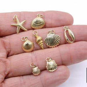 May include: A set of seven gold-tone charms featuring seashells and a starfish. The charms are displayed on a hand.