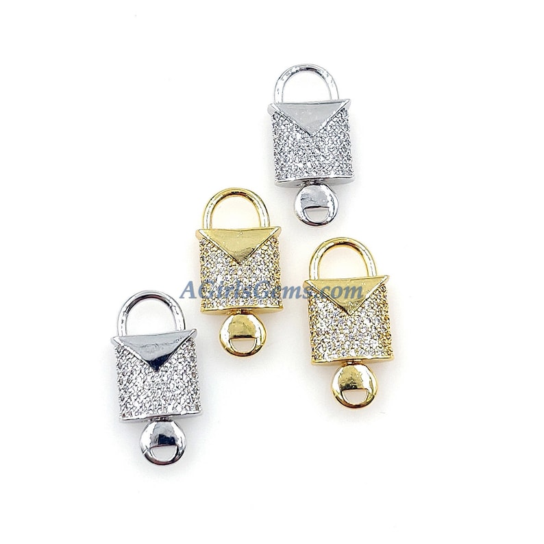 May include: Three silver, gold, and white padlock charms with a clear crystal design. The charms are in the shape of a small handbag with a padlock clasp.