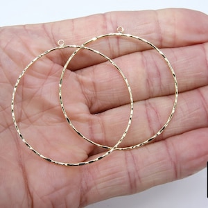Puede incluir: Dos pendientes de aro dorados con un acabado texturizado. Los aros son circulares y tienen un aspecto ligeramente martillado.