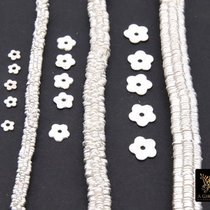 May include: Four strands of silver metal chain with flower-shaped metal beads. The beads are arranged in a row on a black background.