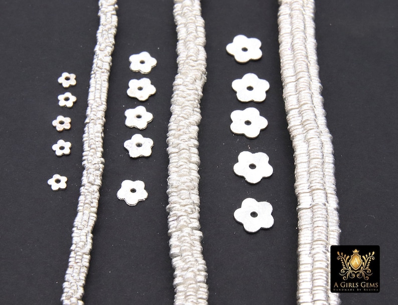 May include: Four strands of silver metal chain with flower-shaped metal beads. The beads are arranged in a row on a black background.