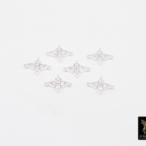 May include: Six silver-coloured, four-pointed star-shaped connectors with clear, round gemstones. Each connector has a central gemstone and smaller stones at each point. The connectors are arranged on a white surface.