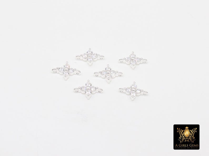 May include: Six silver-coloured, four-pointed star-shaped connectors with clear, round gemstones. Each connector has a central gemstone and smaller stones at each point. The connectors are arranged on a white surface.