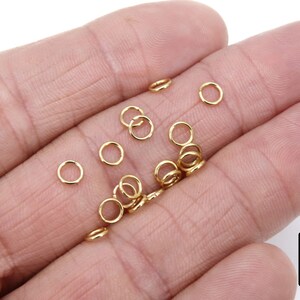 May include: A close-up of a hand holding a group of small, gold jump rings. The rings are about 5mm in diameter and are perfect for jewelry making.