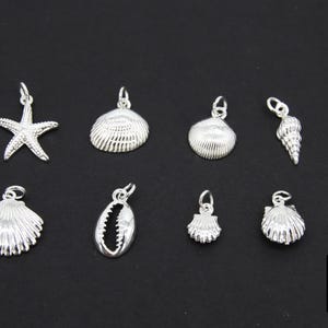 May include: Nine silver charms in the shape of seashells and a starfish. The charms are all different sizes and have a shiny finish.