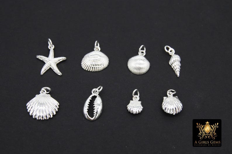 May include: Nine silver charms in the shape of seashells and a starfish. The charms are all different sizes and have a shiny finish.