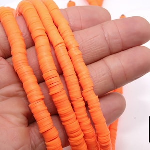May include: A close-up of a strand of bright orange polymer clay beads. The beads are flat and round, and they are strung together on a clear string. The beads are about 1/2 inch in diameter.
