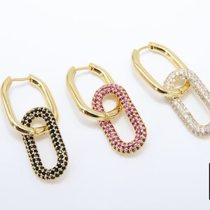 May include: Three pairs of gold hoop earrings with a linked oval design. The ovals are covered in small stones. One pair has black stones, one has pink stones, and one has clear stones.