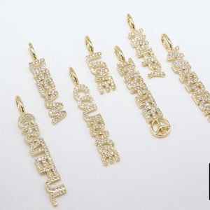 May include: A set of seven gold charm pendants with different words spelled out in sparkling diamonds. The words are "Dream", "Courage", "Love", "Happiness", "Inspired", "Grateful", and "Peace".