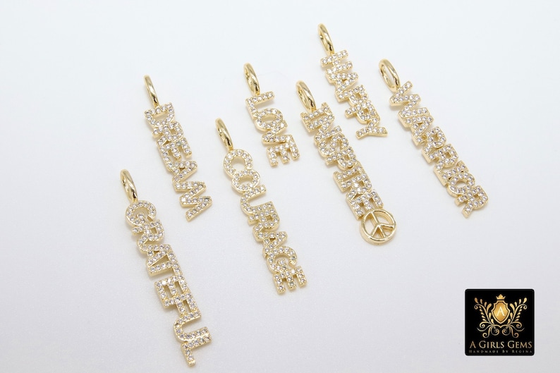 May include: A set of seven gold charm pendants with different words spelled out in sparkling diamonds. The words are "Dream", "Courage", "Love", "Happiness", "Inspired", "Grateful", and "Peace".