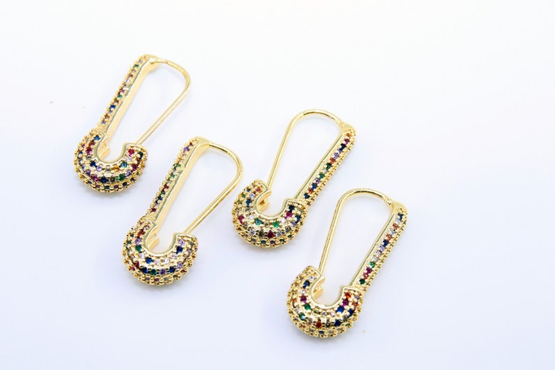May include: Three pairs of gold safety pin earrings with colorful rhinestones. The earrings are a trendy and stylish accessory.