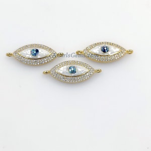 May include: Three gold-tone evil eye charms with white mother of pearl and blue crystal accents. The charms are oval shaped and have a clear crystal halo around the evil eye.