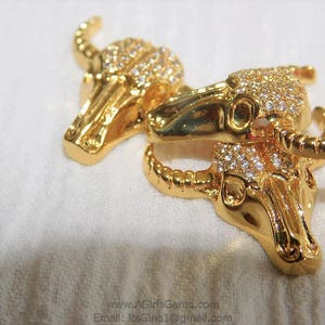 May include: Two gold-tone bull head pendants with clear rhinestones. The pendants are connected by a gold-tone chain.