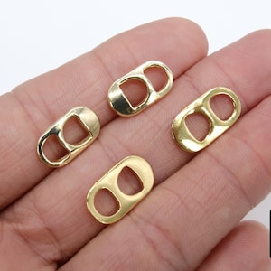 Puede incluir: Se muestran cuatro tiradores de anilla de metal de color dorado, también conocidos como tiradores de apertura, en una mano. Los tiradores son de forma ovalada con dos agujeros en cada uno.