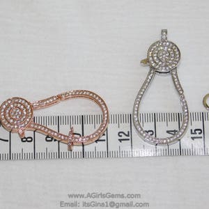May include: Two silver and rose gold tone metal clasps with clear crystal accents. The clasps are about 2 inches long and are shown on a ruler.