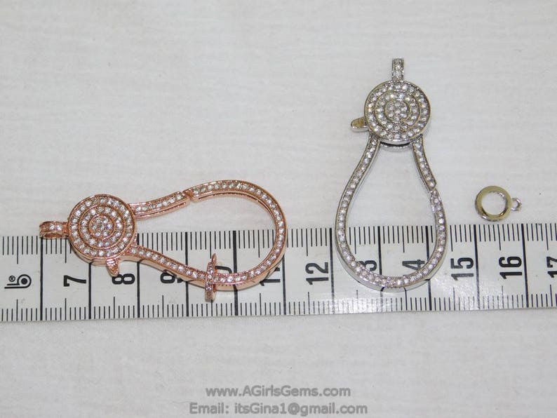 May include: Two silver and rose gold tone metal clasps with clear crystal accents. The clasps are about 2 inches long and are shown on a ruler.