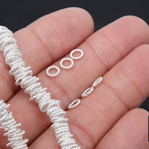 May include: Two silver chains made of twisted wire, with a few small silver jump rings on a hand.