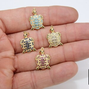 Op de afbeelding: Vier gouden schildpadbedels met verschillende gekleurde edelstenen. De schildpadden zijn bezet met kleine, ronde edelstenen in een pav&eacute;-setting. De kleuren van de edelstenen zijn blauw, wit, rood en lichtblauw.