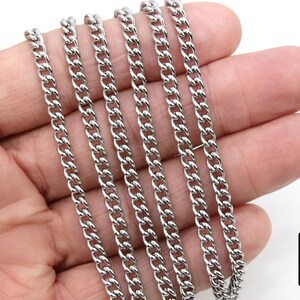 May include: A close-up of a silver curb chain necklace. The chain is laid out in a straight line on a hand, showing the detail of the links.