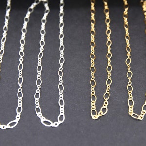 May include: Two chains, one silver and one gold, are shown against a black background. Both chains are made of oval links.