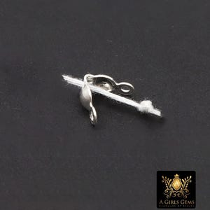 May include: A silver-colored jewelry clasp attached to a white string, set against a dark background. The clasp has a curved design with a loop and a hook. The image also includes a logo in the bottom right corner.