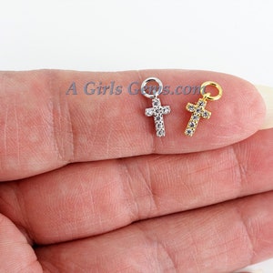 May include: Two small cross charms, one silver and one gold, both with clear cubic zirconia stones.